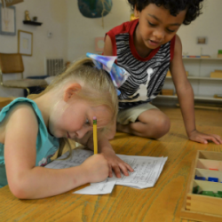 Two children sitting at a table writing with a pencil on paper