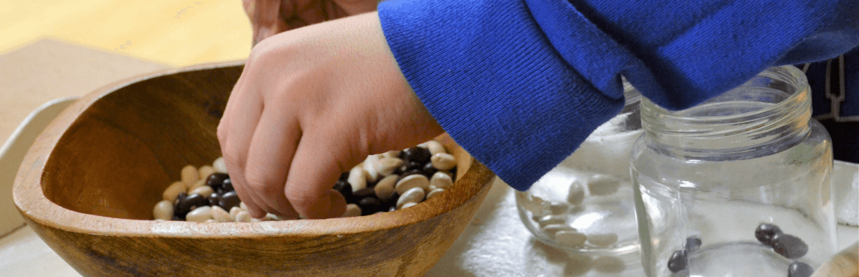 Child's hand reaching into a bowel with white and black dry beans in it